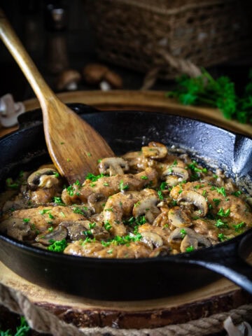 Pan of Chicken Marsala being stirred with a wooden spatula.